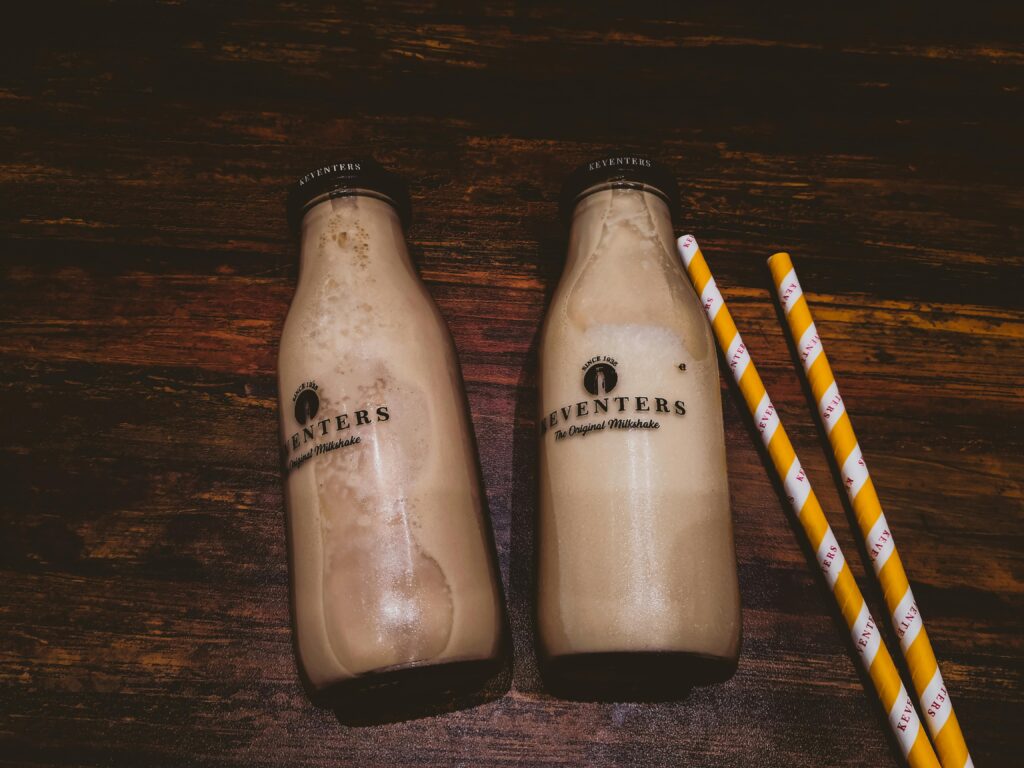 Two bottles of creamy milkshakes with straws on wooden background.