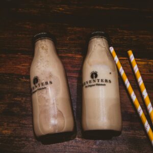 Two bottles of creamy milkshakes with straws on wooden background.