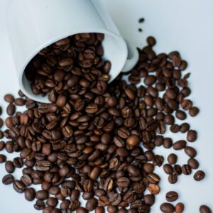 A white mug tipped over, spilling roasted coffee beans on a white surface.