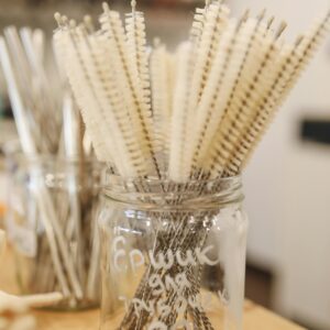 Reusable cleaning brushes and metal straws in a glass jar promoting zero waste lifestyle.