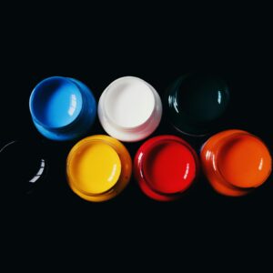 Top view of vibrant acrylic paints in jars on a black background, showcasing bold colors.