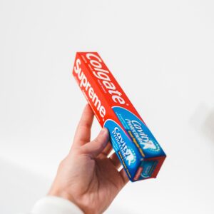 Close-up of a hand holding a Colgate toothpaste box against a white background.