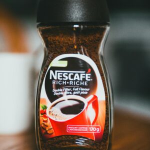 Closeup of glass jar with colorful logotype and with instant coffee placed on wooden brown table