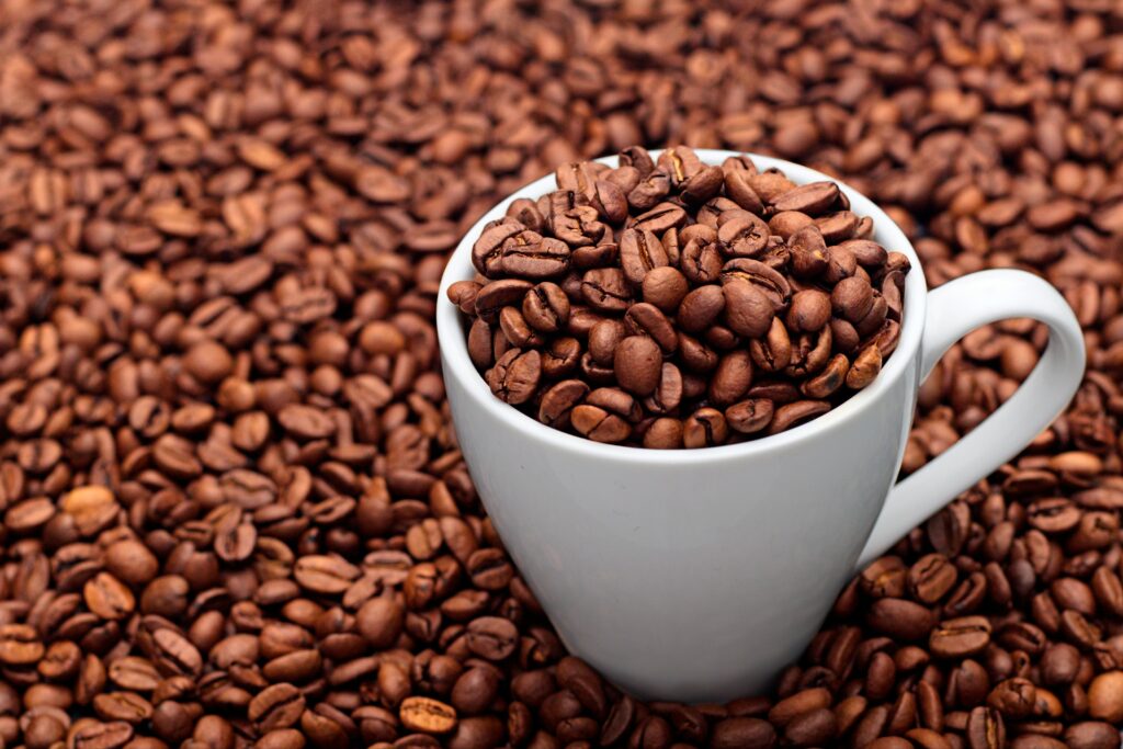 A white ceramic mug full of coffee beans surrounded by a background of coffee beans, showcasing a rich coffee theme.